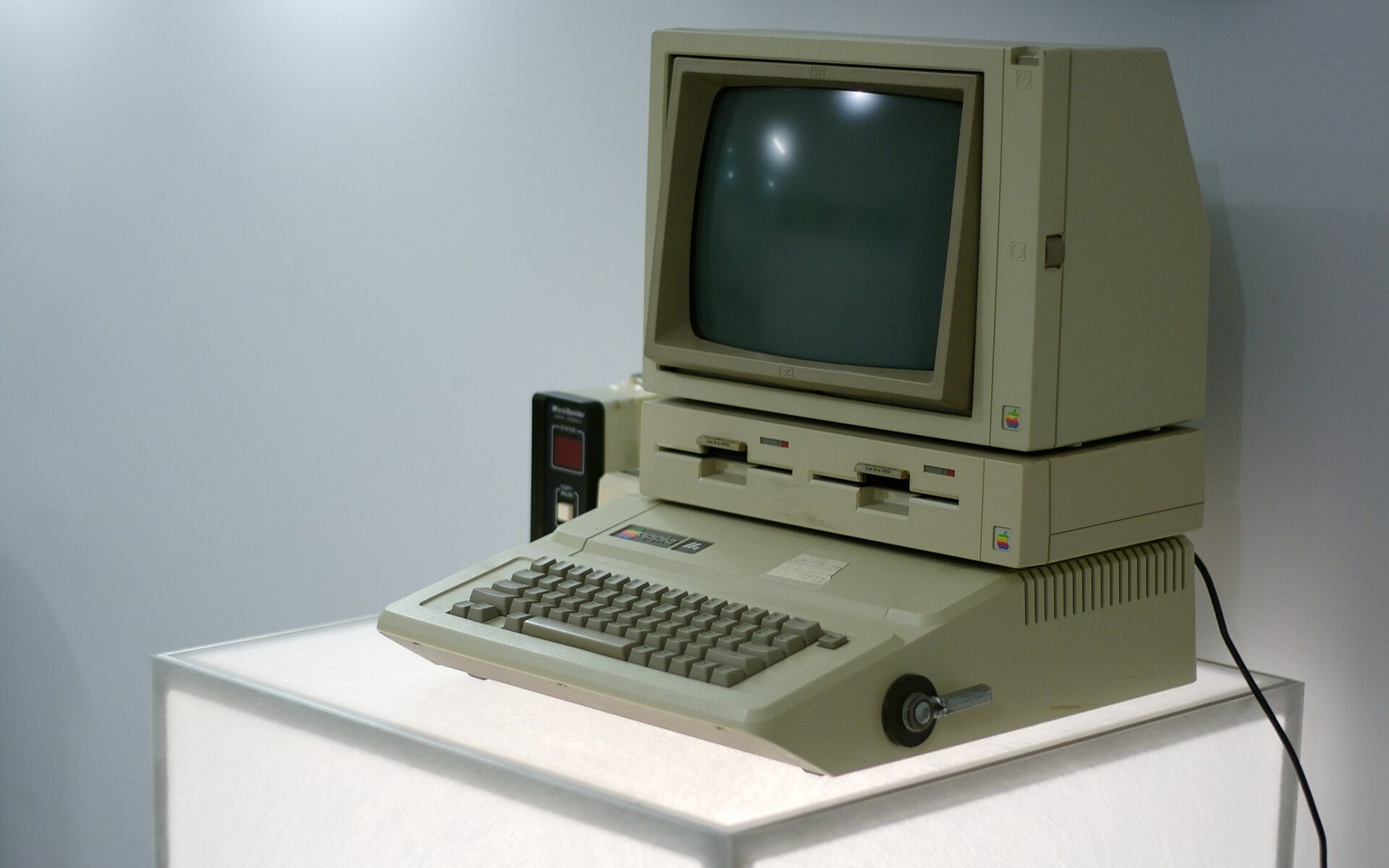 Vintage Apple IIe computer with dual floppy drives displayed on a white pedestal