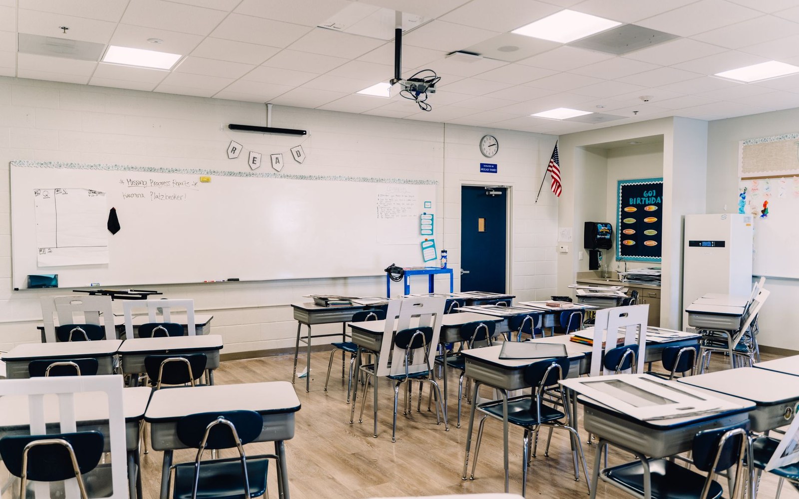 Empty classroom with rows of student desks facing a whiteboard and ceiling projector