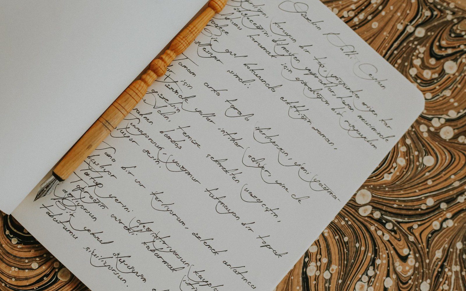 Handwritten cursive notebook page with a wooden fountain pen resting on the paper