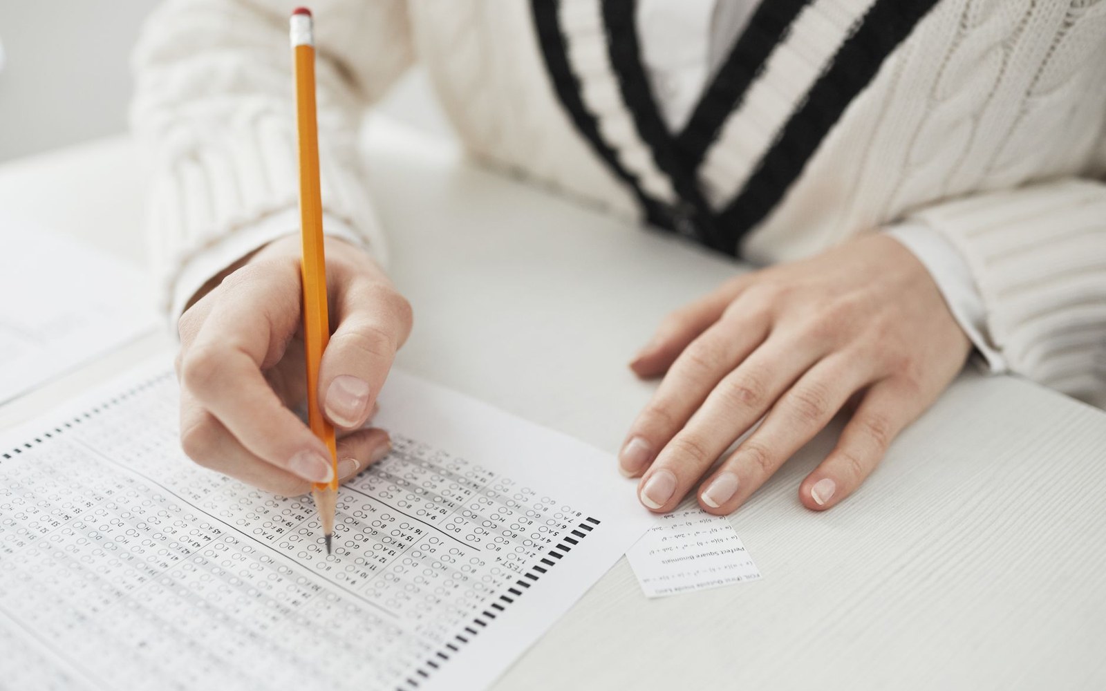 Hands filling in bubbles on a multiple-choice answer sheet with a pencil